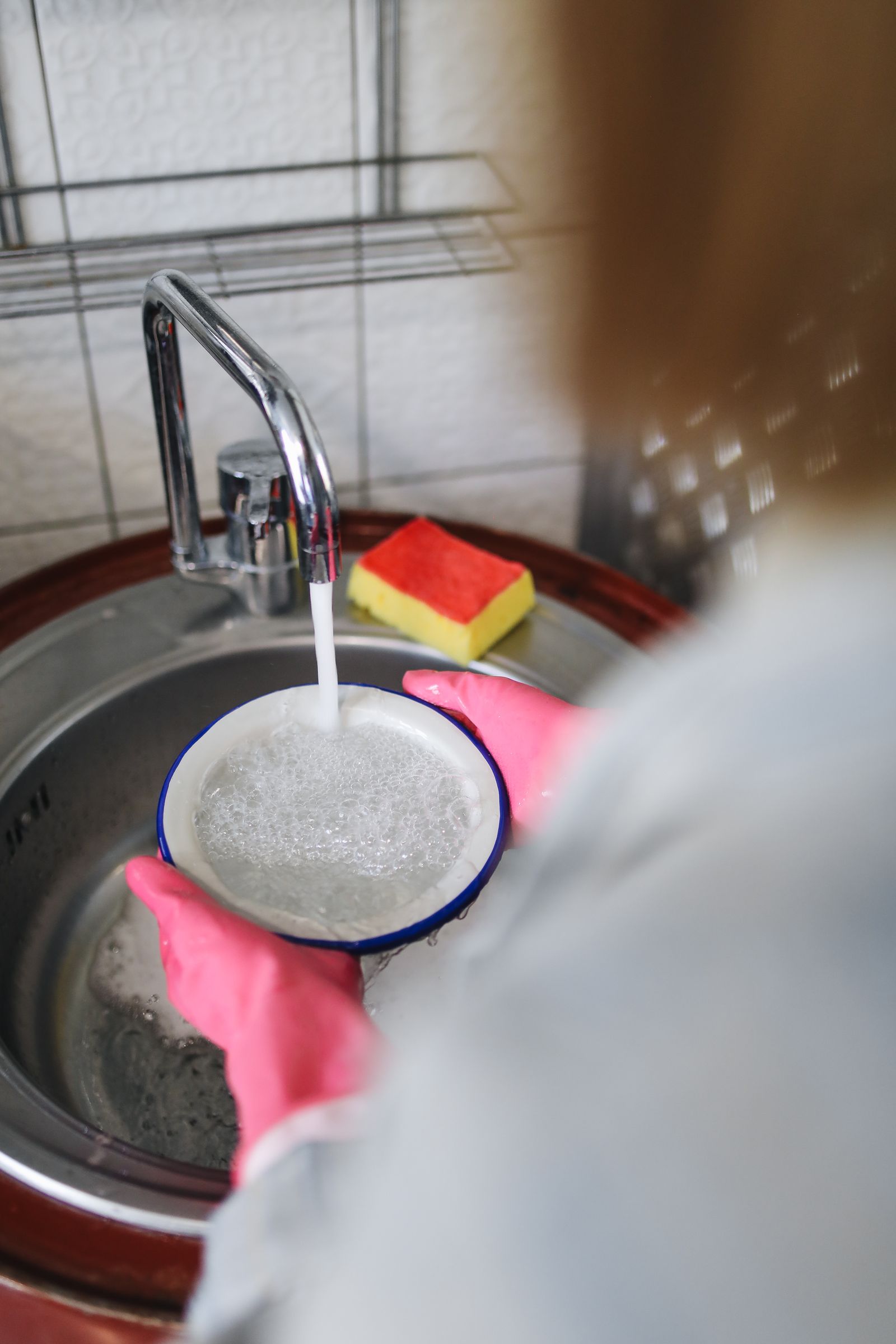 Gloved hands washing a ceramic bowl in a sink